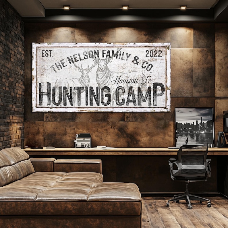 May include: A white sign with black text and a drawing of two deer. The sign reads "EST. THE NELSON FAMILY & CO. 2022 Houston, Tx HUNTING CAMP".