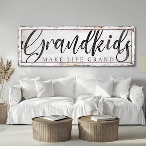 May include: White wooden sign with black text that reads "Grandkids Make Life Grand". The sign is hanging on a white wall above a white couch.