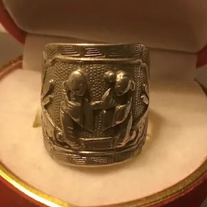 Peut inclure: Bague en argent avec un motif complexe de deux personnages en costume traditionnel. La bague est présentée dans un écrin en velours rouge.