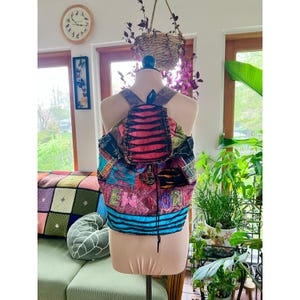 May include: A multicolored patchwork backpack featuring denim and fabric panels in shades of pink, blue, and black. The flap has a black and red striped pattern, and the lower section displays the text NEW YORK in embroidered letters.