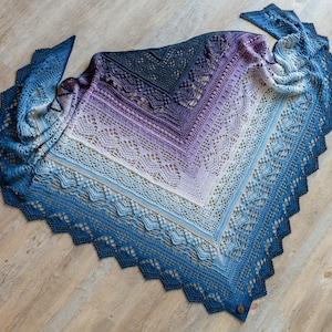 Può includere: Uno scialle fatto a mano nei toni del blu, viola e bianco, con un delicato motivo a pizzo. Lo scialle ha un bordo smerlato e una chiusura con bottone. La sfumatura di colore passa dal blu scuro al blu chiaro e al viola.