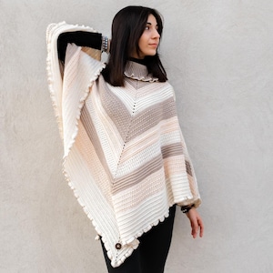 May include: A crocheted poncho with a striped pattern in shades of beige, cream, and pink. The poncho has a ruffled edge and a button closure.