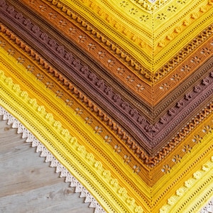 May include: A crocheted shawl with a gradient of yellow, orange, and brown colors. The shawl has a delicate lace border.