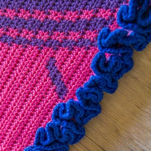 May include: A crocheted blanket with a pink and purple striped pattern and a blue ruffled border.