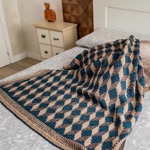 May include: A crocheted throw blanket with a diamond pattern in shades of brown and teal. The blanket is draped over a bed with a white headboard.