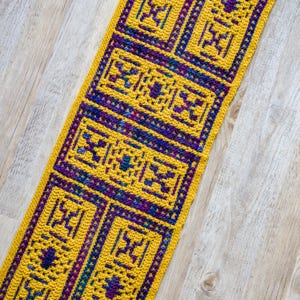 Può includere: Un runner all'uncinetto giallo e viola con un motivo geometrico. Il runner è realizzato con un filato spesso e ha una superficie testurizzata.