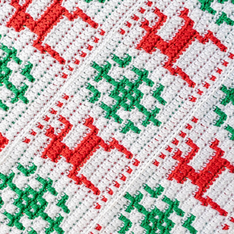 May include: A white crocheted blanket with a repeating pattern of red and green reindeer. The blanket is made with a simple stitch and has a soft, textured feel.