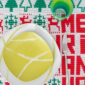 May include: A white square plate with a green square plate inside. The plates are on a white and red crocheted tablecloth with a green and white pattern.