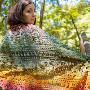 May include: A woman wearing a crocheted shawl with a rainbow ombre color pattern. The shawl is made with a delicate open stitch design and features a variety of colors, including pink, green, yellow, and orange.