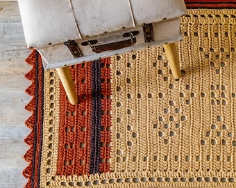 May include: A crocheted rug with a brown, orange, and beige color scheme. The rug has a geometric pattern and a fringe border. A wooden stool with a light brown fabric top sits on the rug.