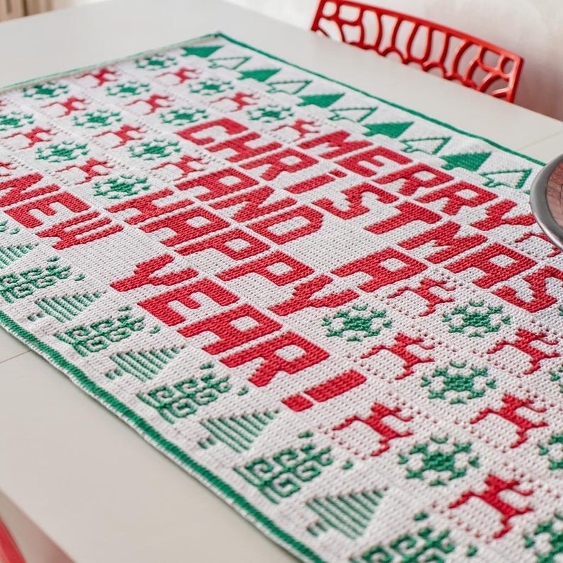 May include: A white crocheted table runner with a green and red Christmas design. The runner features the text "Merry Christmas and Happy New Year!" in red.