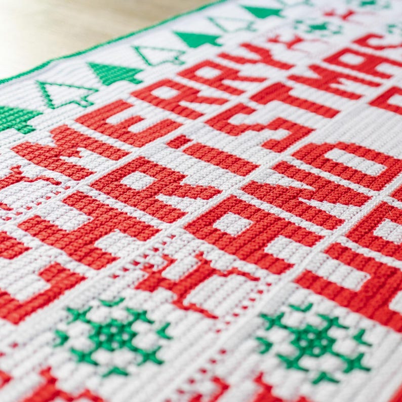 May include: White crochet blanket with red lettering that says "Merry Christmas". The blanket has a green border with small green Christmas trees and snowflakes.