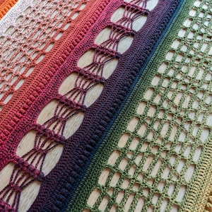 Può includere: Primo piano di una coperta all'uncinetto fatta a mano con una sfumatura di colori. La coperta passa dall'arancione al rosso, al viola, al verde e al giallo. Il design include trafori e punti strutturati, creando una superficie visivamente accattivante e tattile.