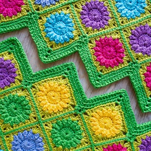 May include: A crocheted blanket with a zig-zag pattern. The blanket is made of squares in various colours, including green, yellow, blue, pink, and purple.
