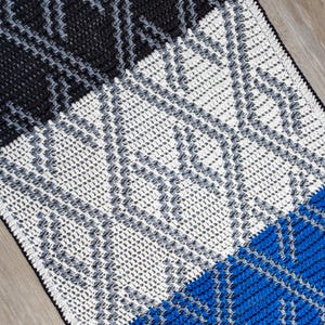 May include: A crocheted blanket with a geometric pattern in shades of black, white, gray, and blue.