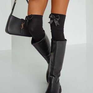 Op de afbeelding: Zwarte kniehoge laarzen met een dikke hak en een zwarte leren handtas met een gouden YSL-logo.