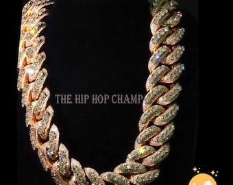 May include: A gold chain necklace with a large, intricate design. The chain is covered in small, sparkling diamonds. The chain is on a black background. The text "THE HIP HOP CHAMP" is visible in the image.