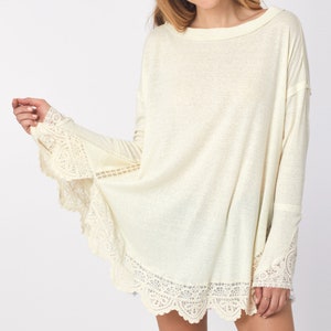 May include: A white, long-sleeved, loose-fitting top with a round neckline and lace trim around the sleeves and hem.