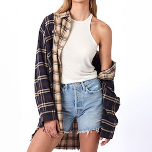 May include: A woman wearing a white tank top, blue denim shorts, and a blue and brown plaid shirt tied around her waist.