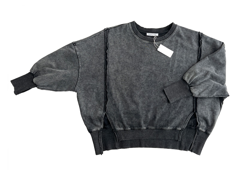 May include: A dark gray, oversized sweatshirt with a distressed look. The sweatshirt has a round neckline and long sleeves with a gathered detail at the shoulders. The sweatshirt has a raw edge detail at the hem and sides.