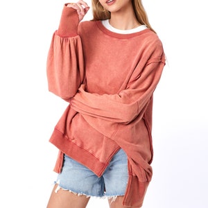 May include: A terracotta-colored oversized sweatshirt with a relaxed fit and long sleeves. The sweatshirt has a slightly distressed look and a high, round neckline.