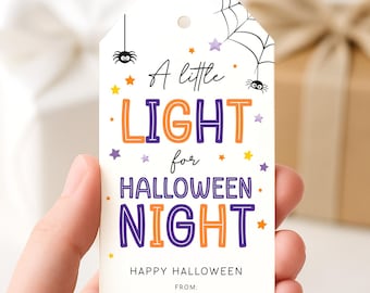 May include: A white Halloween gift tag with the text "A little LIGHT for HALLOWEEN NIGHT". The tag features orange and purple stars, spiders, and a spiderweb design. The words "HAPPY HALLOWEEN" are also printed on the tag.