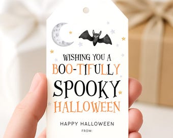Op de afbeelding: Een witte Halloween-cadeaulabel met een aquarel illustratie van een halve maan, sterren en een vleermuis. De label leest "Wishing you a Boo-tifully Spooky Halloween" in zwarte en oranje tekst. "Happy Halloween" en "From:" staan ook op de label.