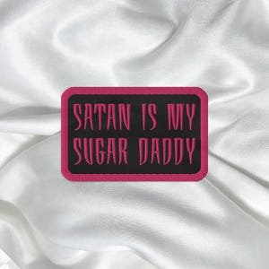 May include: A black and pink embroidered patch with the text "Satan is my Sugar Daddy".