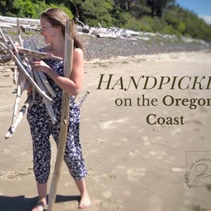 Peut inclure: Une personne tenant du bois flott&eacute; sur une plage de sable. Le texte "HANDPICKED on the Oregon Coast" est affich&eacute; en marron. L'image comprend &eacute;galement un logo pour "The Forest & Cove".