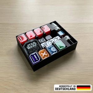 Könnte beinhalten: Ein schwarzes, rechteckiges Aufbewahrungstablett mit verschiedenen Star Wars Unlimited Spielmarken und Würfeln. Das Tablett verfügt über Fächer für rote Schadensmarker, weiße Modifikatorwürfel sowie bunte Acryl-Spielsteine mit Symbolen und Text.