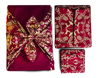 Könnte beinhalten: Drei rote und goldene Stoff-Geschenkpapierquadrate mit einem goldenen Blumenmuster. Das größte Quadrat ist mit einer Schleife gebunden und trägt den Text "CARIDE" in goldenen Buchstaben. Die kleineren Quadrate sind zu einer quadratischen Form gefaltet.