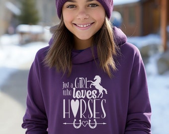 May include: Purple hoodie with a white graphic that says "Just a Girl who loves Horses" with a heart and horseshoes. The model is wearing a purple beanie with a pom pom.