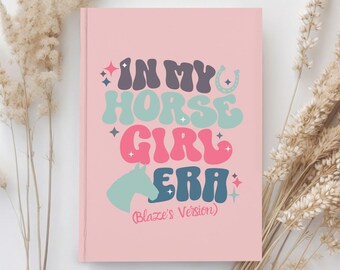 May include: Pink notebook with the text "In My Horse Girl Era (Blaze's Version)" in a retro font with a horse silhouette and stars.