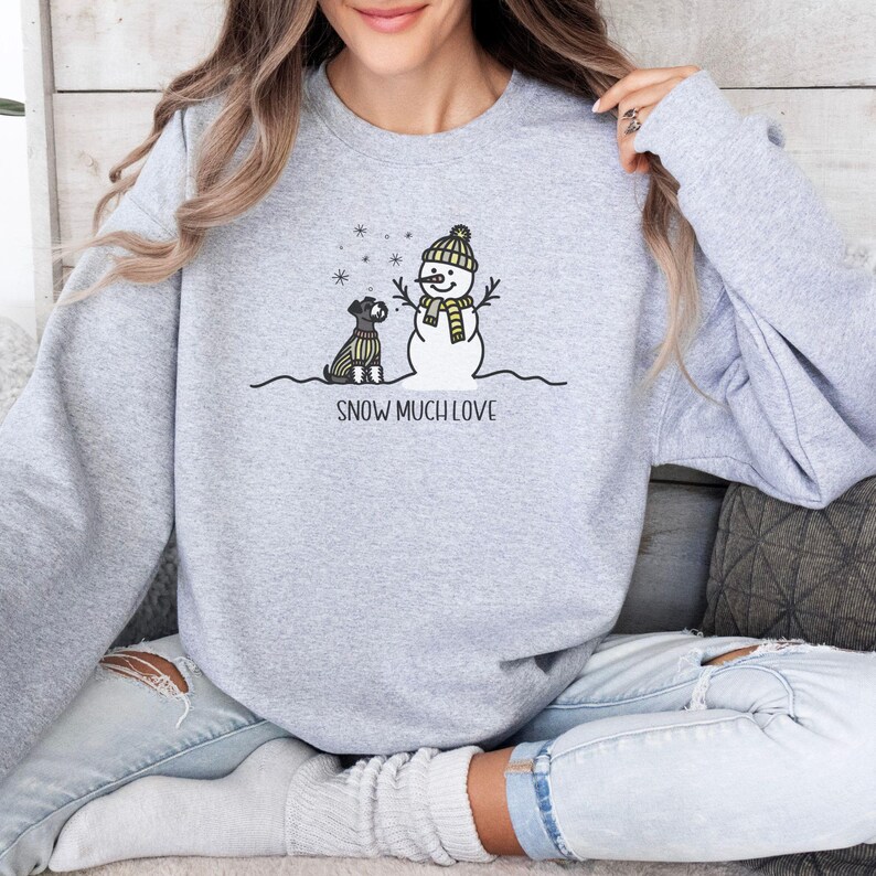 May include: A gray sweatshirt with a snowman and a dog wearing a scarf. The text "SNOW MUCH LOVE" is printed below the image.
