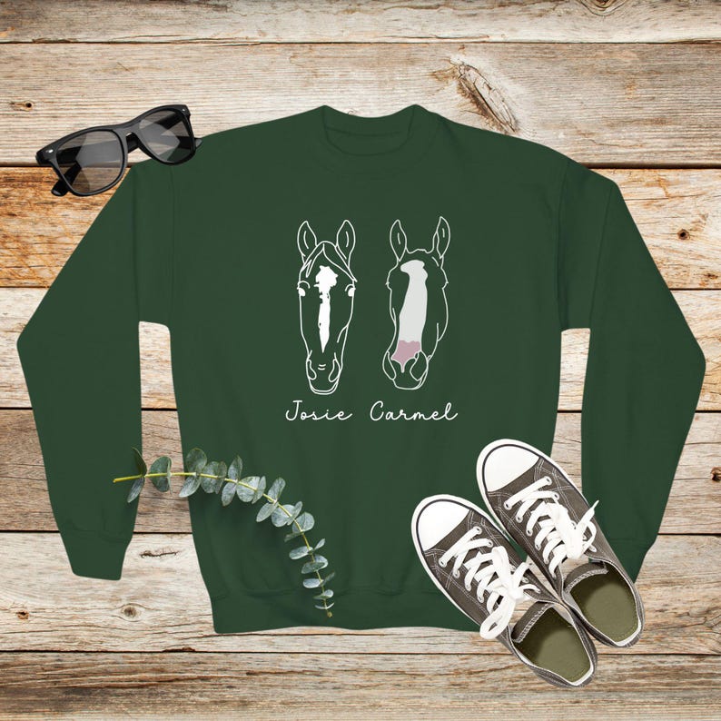 May include: A dark green sweatshirt with a white outline of two horse heads and the names "Josie" and "Carmel" printed on the front.