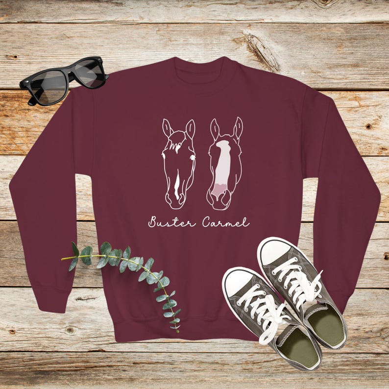 May include: Burgundy sweatshirt with a white outline of two horse heads and the text "Buster Carmel" printed on the front.