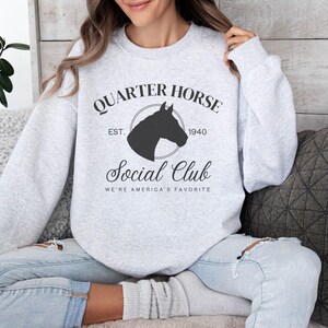 May include: A gray sweatshirt with a black silhouette of a horse's head in a circle. The text "Quarter Horse Social Club Est. 1940 We're America's Favorite" is printed on the sweatshirt.