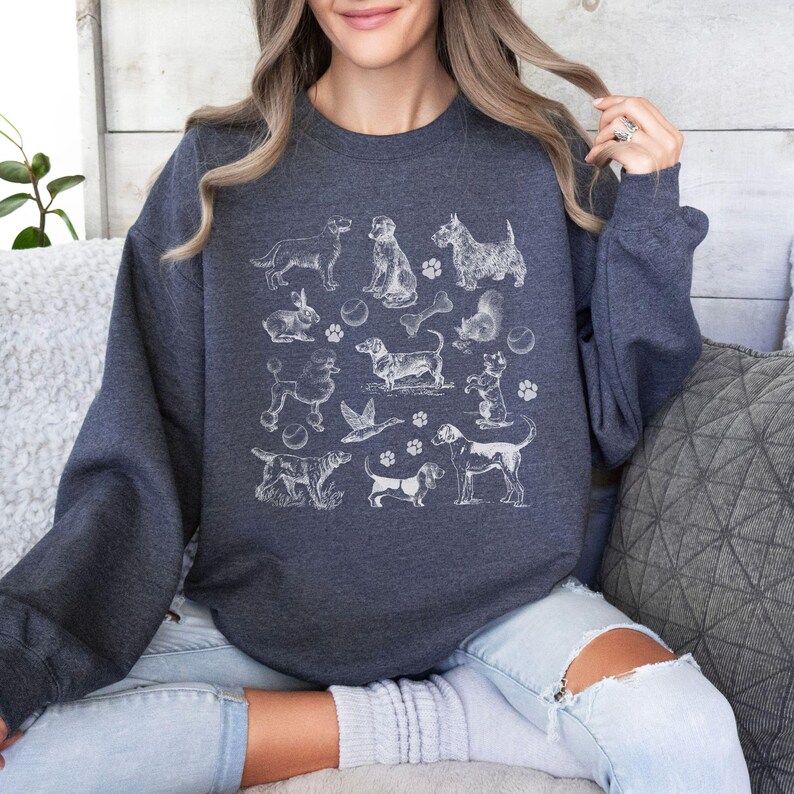 Peut inclure: Un sweat-shirt bleu marine avec un imprim&eacute; graphique blanc de diff&eacute;rentes races de chiens et accessoires. Le graphique comprend un os, une balle, un &eacute;cureuil et un canard.