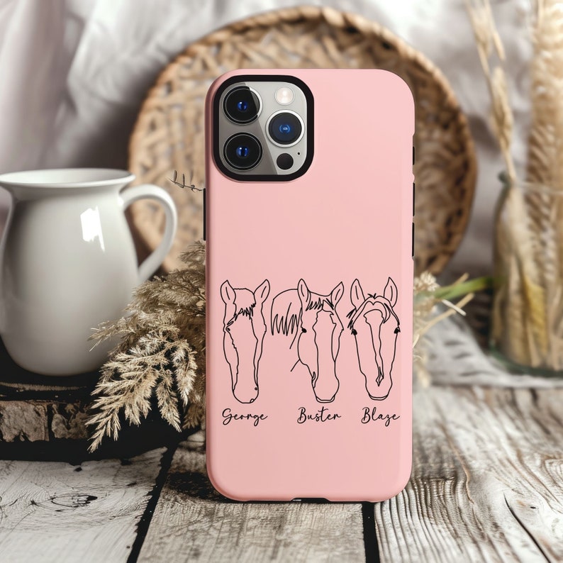 May include: Pink phone case with a black outline of three horse heads and the names George, Buster, and Blaze underneath.