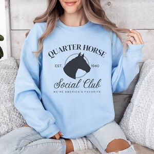 May include: Light blue sweatshirt with a black graphic of a horse's head in a circle with the text "Quarter Horse Social Club Est. 1940 We're America's Favorite"