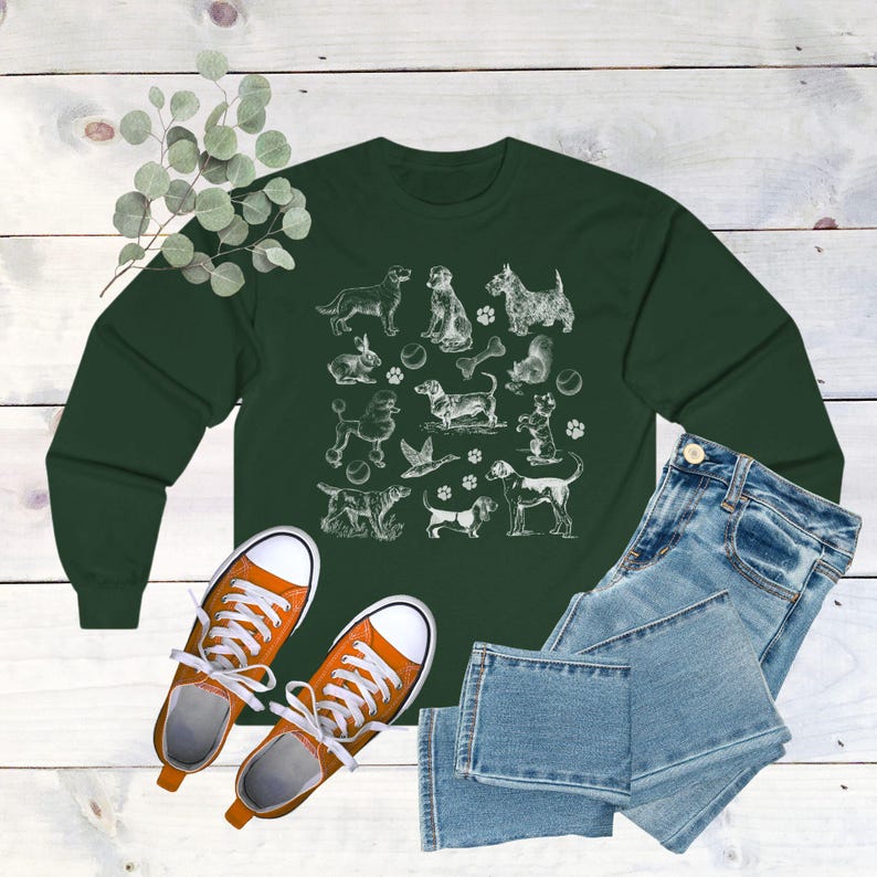 May include: A dark green long-sleeved shirt with a white graphic print of various dog breeds and paw prints. The shirt is paired with blue jeans and orange sneakers.
