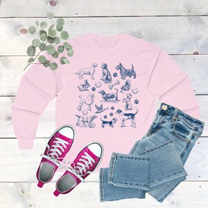 May include: A pink long-sleeved sweatshirt with a blue and white print of various dogs, a rabbit, a squirrel, and other animals. The print includes bones, balls, and paw prints.