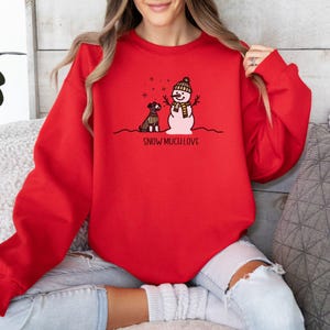 May include: Red sweatshirt with a snowman and a dog graphic. The text "SNOW MUCH LOVE" is printed below the graphic.