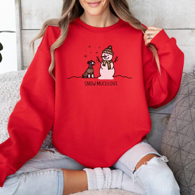 May include: Red sweatshirt with a snowman and a dog graphic. The text "SNOW MUCH LOVE" is printed below the graphic.