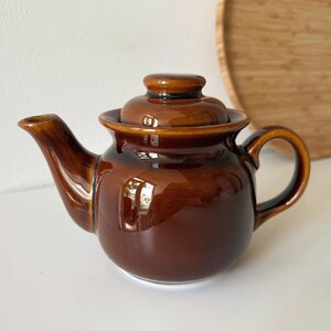 Op de afbeelding: Een witte keramische mok met een zwarte handgreep en de tekst "But First, Coffee" in een handschriftstijl. De mok is bedoeld voor warme dranken en heeft een glanzende afwerking.