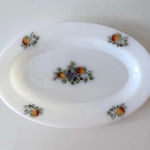 May include: Oval white serving platter with fruit illustrations. The platter features a central design of pears, grapes, and apples, with additional fruit clusters at each corner. A decorative piece for serving food.