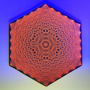 Puede incluir: Una pieza de arte de cuerda hexagonal con un diseño geométrico rojo sobre un fondo negro. El diseño es un patrón complejo de líneas que se cruzan y crean una forma circular en el centro.