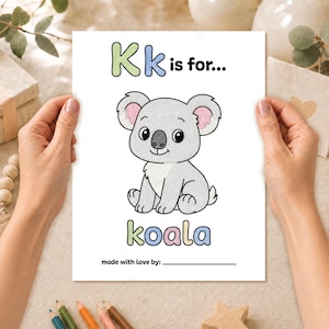 Hands holding a completed K is for koala coloring page from a printable baby shower ABC keepsake book, colored with pencils.