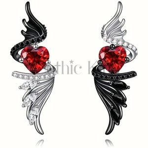 May include: A pair of earrings featuring a red heart with black and white angel wings. One earring has black wings with white accents, and the other has white wings with black accents.