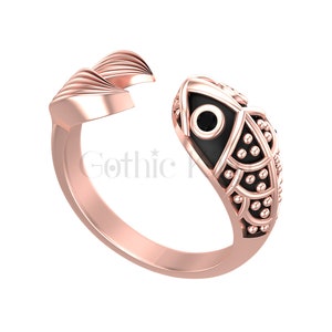 Può includere: Un anello in oro rosa con un design a forma di pesce nero. Il pesce ha un occhio nero con un punto bianco al centro. L'anello è un pezzo di dichiarazione e sarebbe un ottimo regalo.
